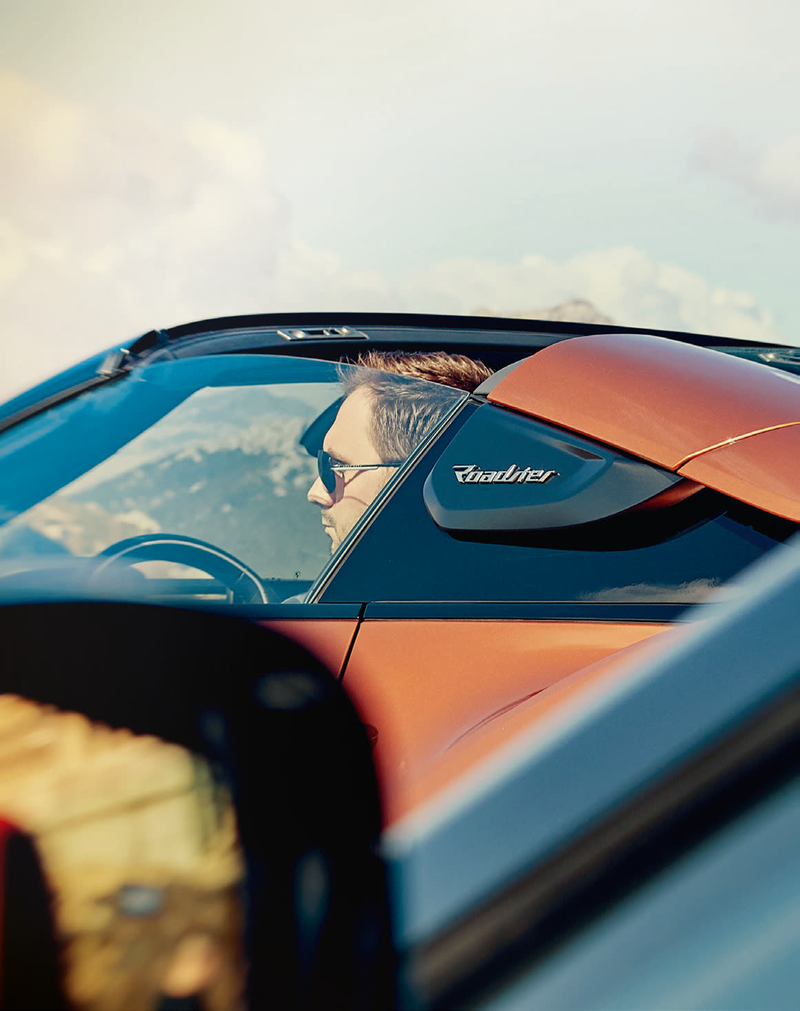 Fahrer im offenen i8 Roadster unter blauem Himmel