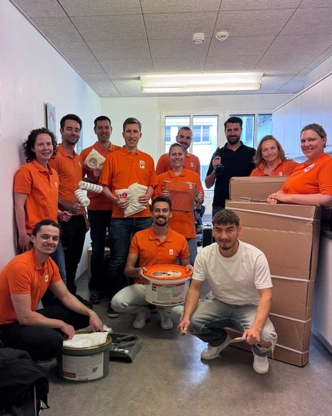 Gruppe in orangefarbenen Shirts mit einer Spendenkiste