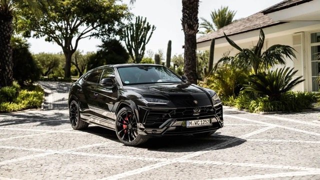 Schwarzer Lamborghini Urus auf einem Parkplatz unter Palmen