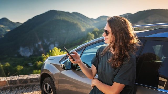 Frau am geöffneten Autofenster auf einer Straße in den Bergen
