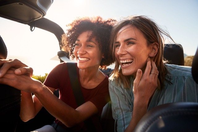 Zwei Frauen lachen aus einem offenen Fahrzeug heraus