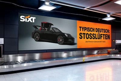Gepäckband mit Sixt-Werbung „Typisch deutsch: Stoßlüften“